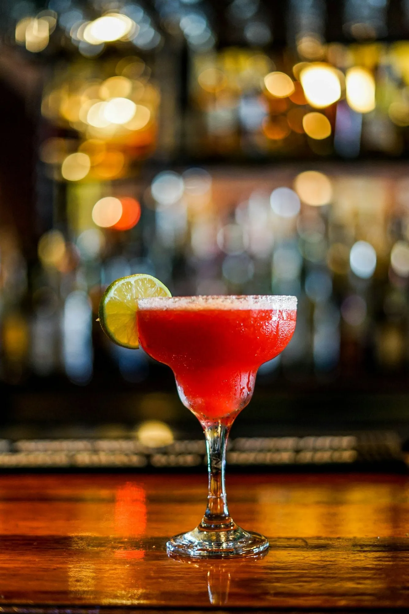 Ruby cocktail with a lime garnish on a bar counter with warm bokeh lights