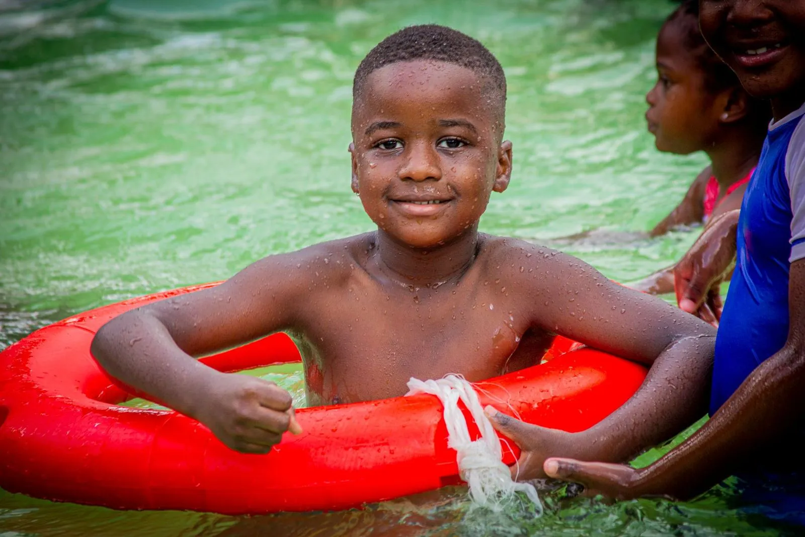 Smiling boy in a red swim ring splashing in the pool