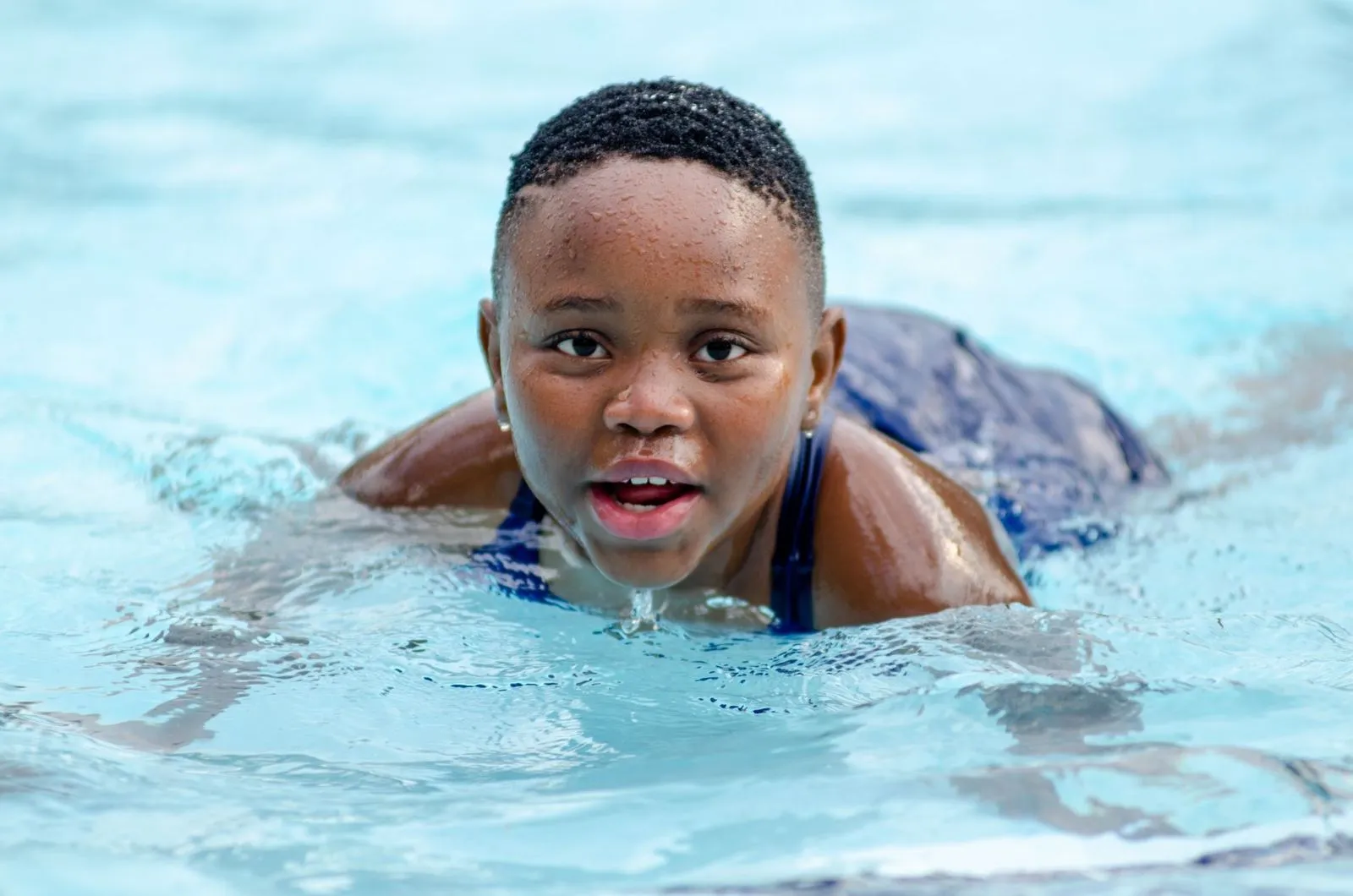 Child swimming towards the camera in a bright outdoor pool