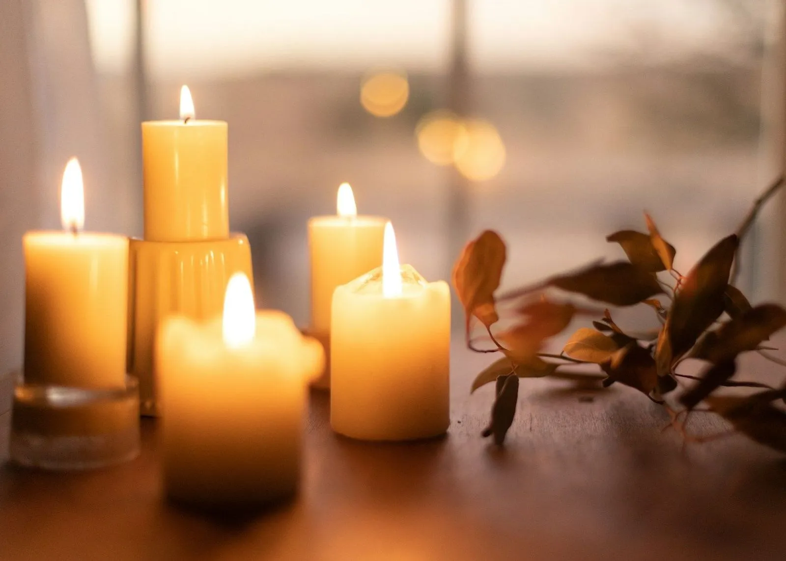 Warm glowing pillar candles on a wooden table with dried leaves